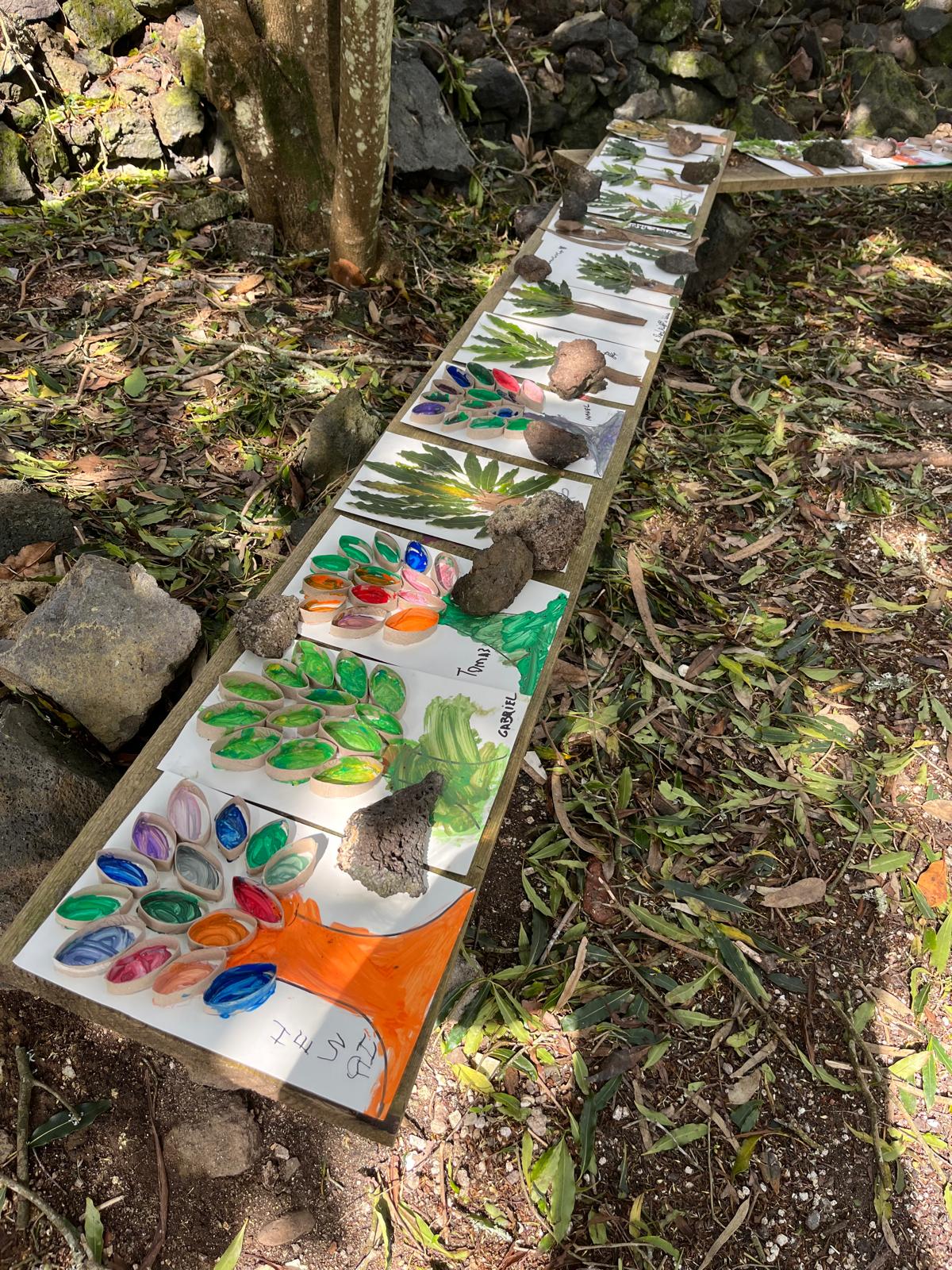 Trabalhos artísticos das crianças expostos num banco de madeira na mata